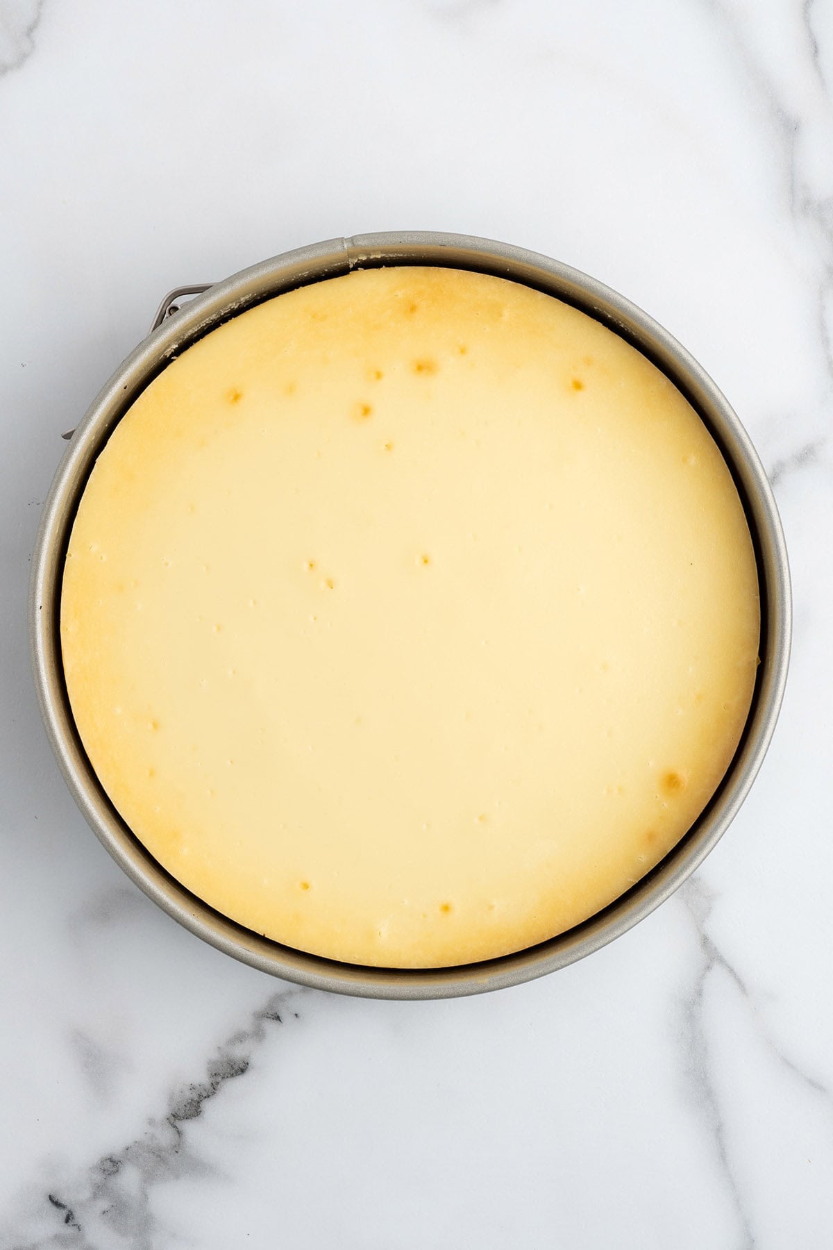 Overhead view of a freshly baked cheesecake with a golden top, still in its springform pan.