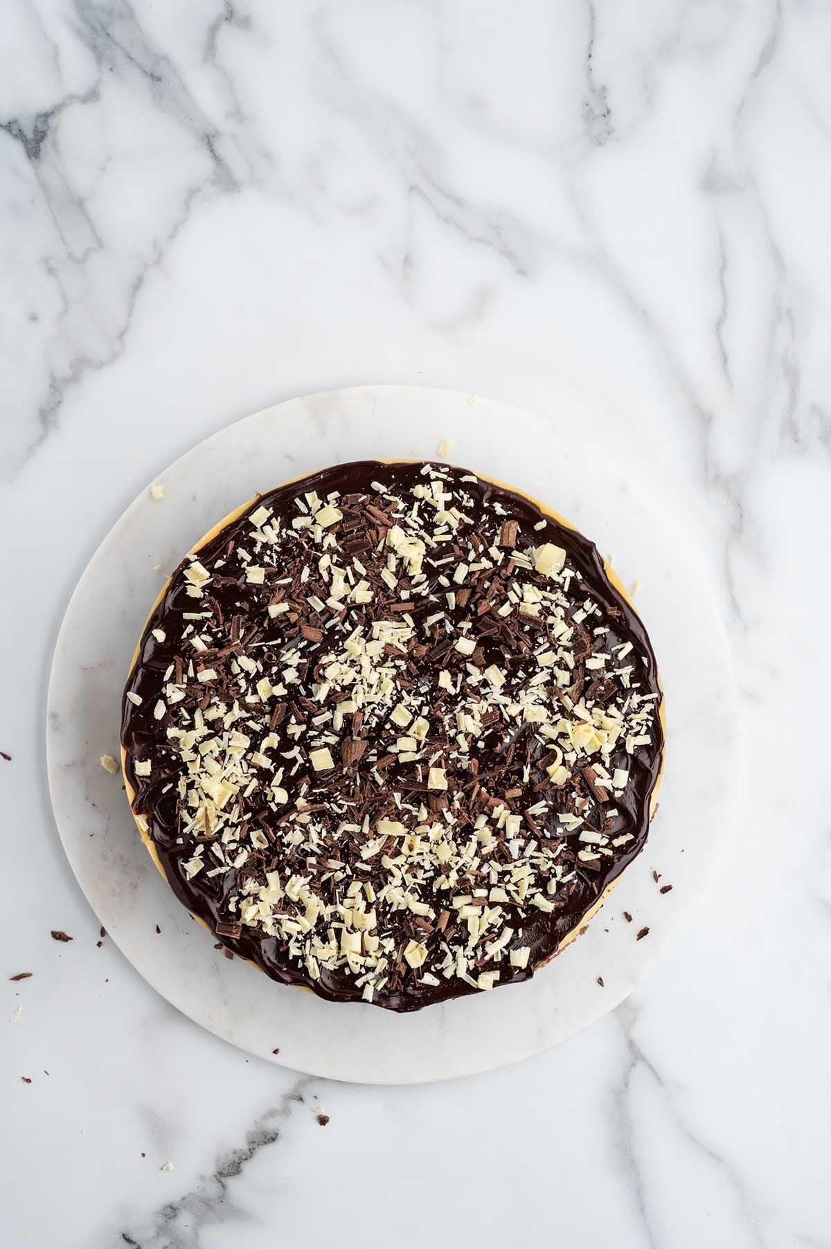 Overhead view of a whole cheesecake topped with chocolate ganache and white and dark chocolate shavings.