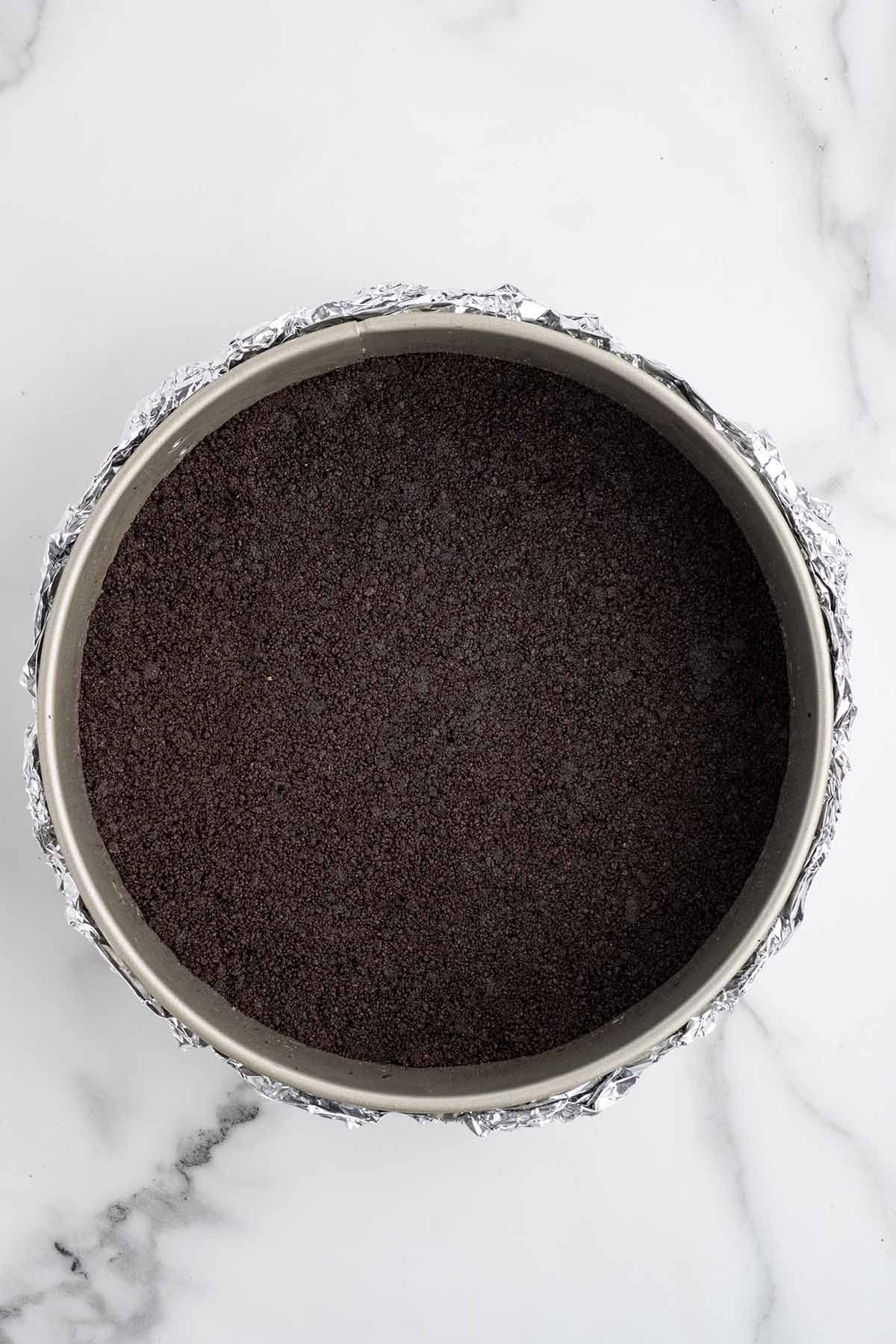Overhead view of an Oreo cookie crust pressed into a foil-wrapped springform pan.