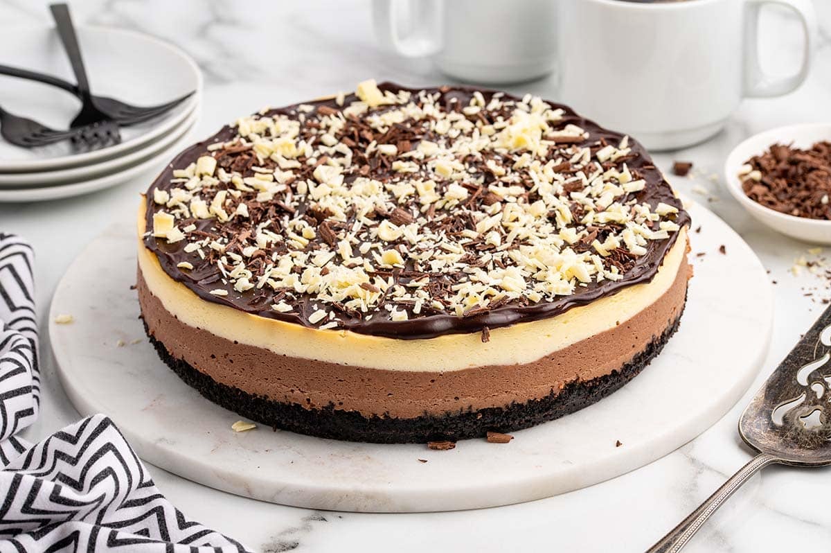Whole layered chocolate cheesecake with Oreo crust and chocolate ganache topping, garnished with white and dark chocolate shavings.