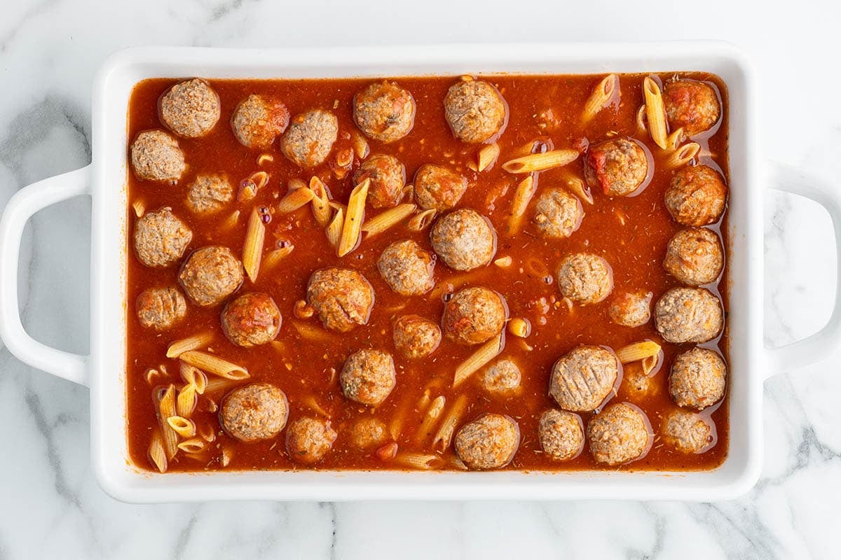 Meatballs, pasta, and marinara sauce combined in a white baking dish before baking.