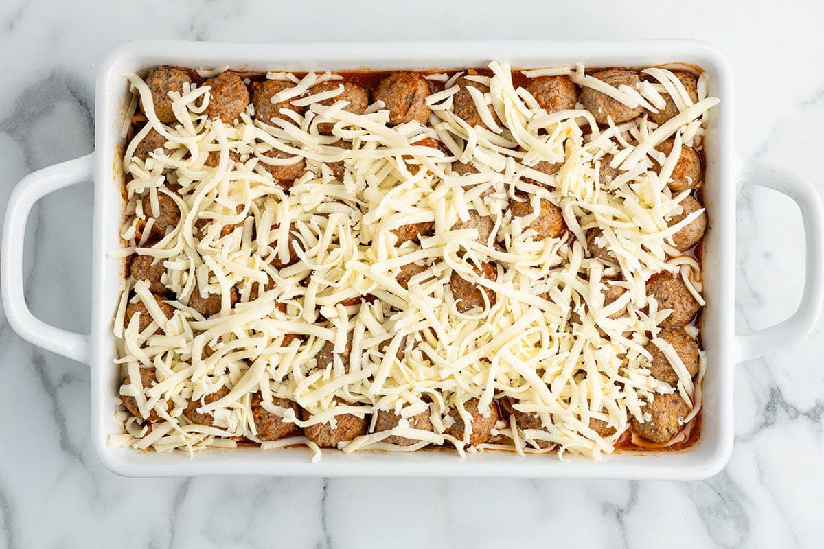Meatball casserole topped with shredded mozzarella cheese before baking.