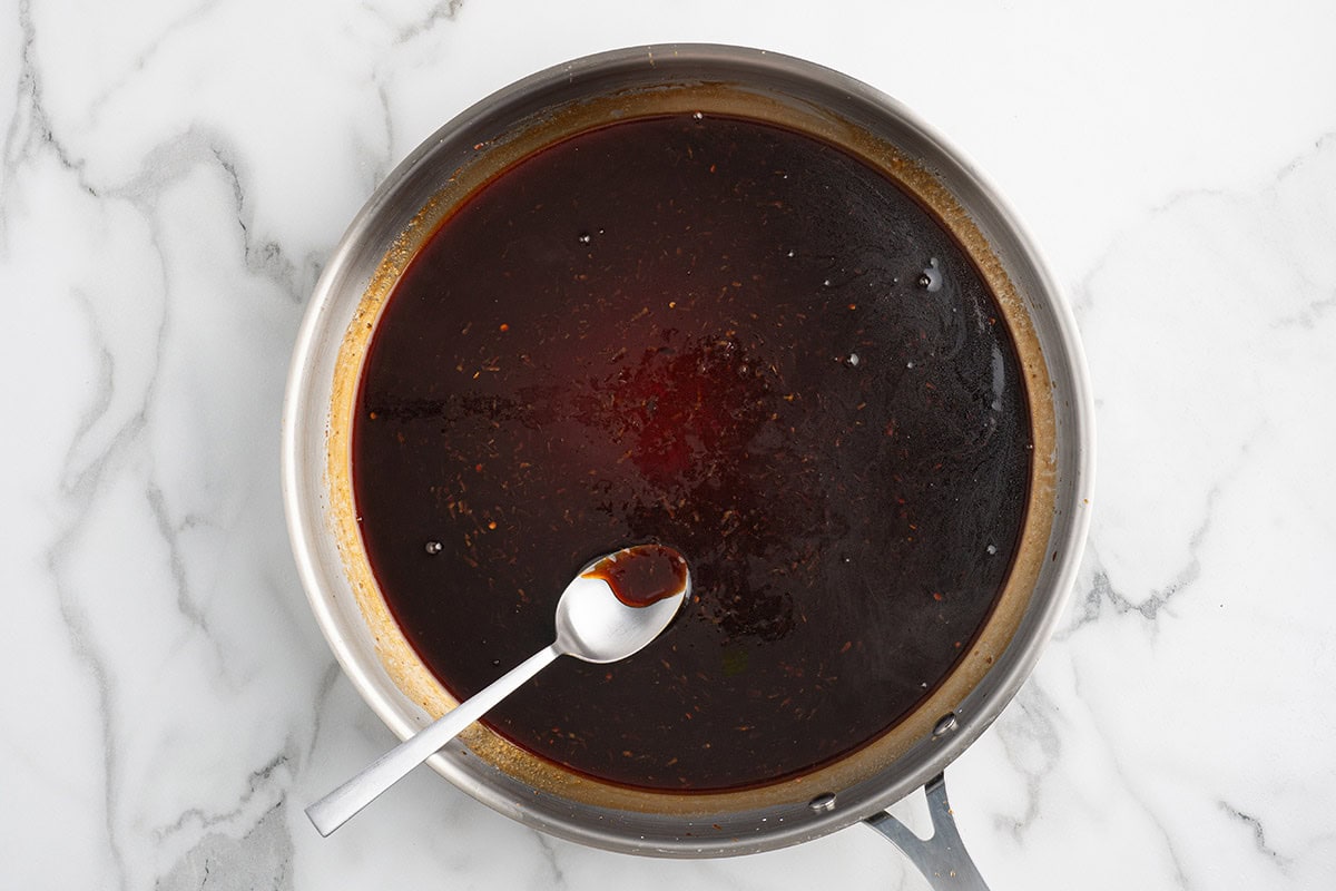 Dark savory sauce simmering in a stainless steel skillet with a spoon.