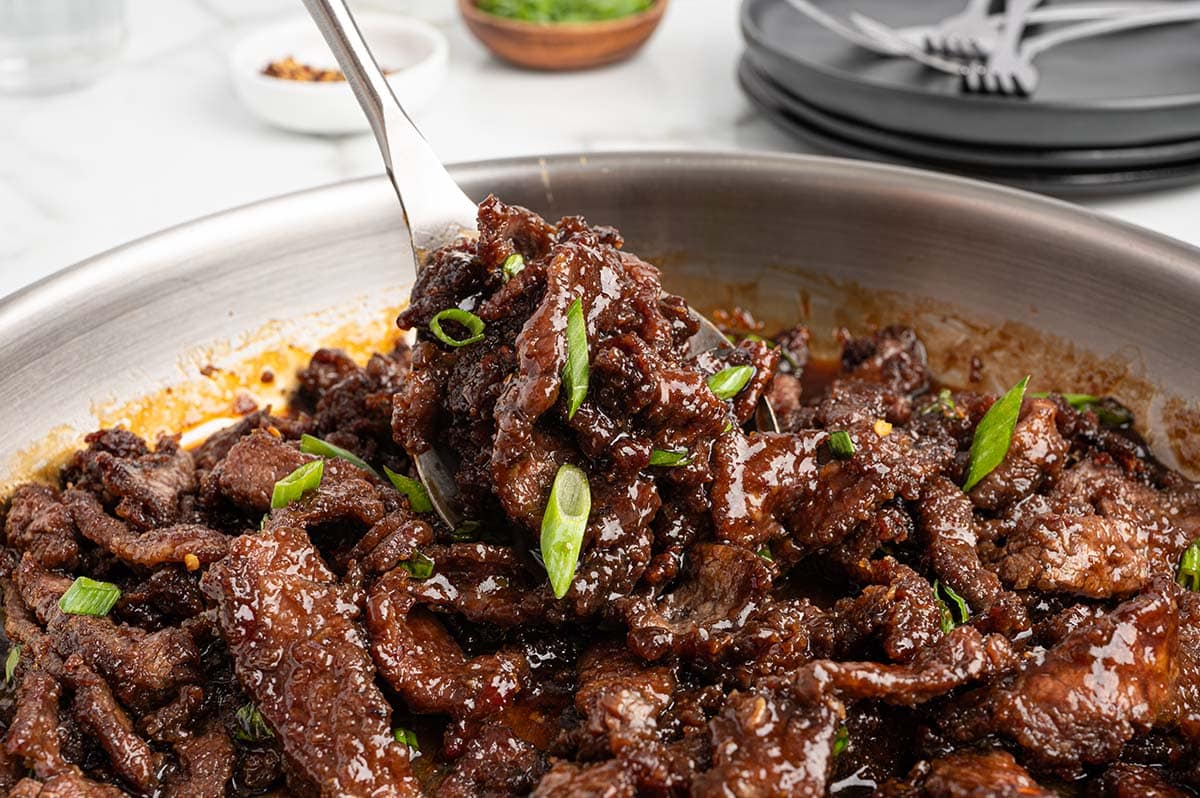 a spoonful mongolian beef lifted up from skillet.