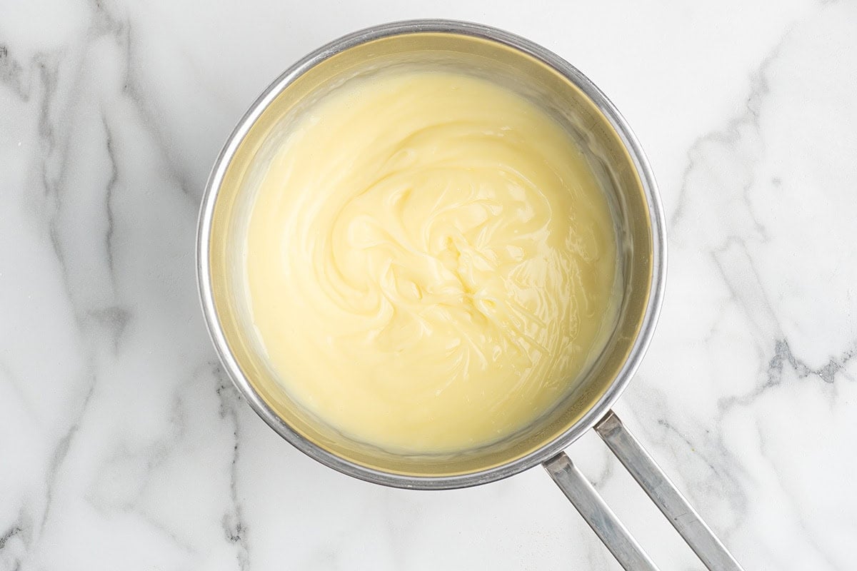 Pastry cream mixture being whisked in a saucepan.