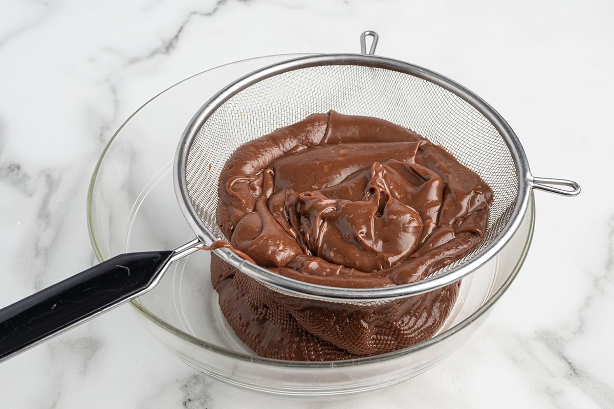 Chocolate custard being strained through a sieve into a bowl.