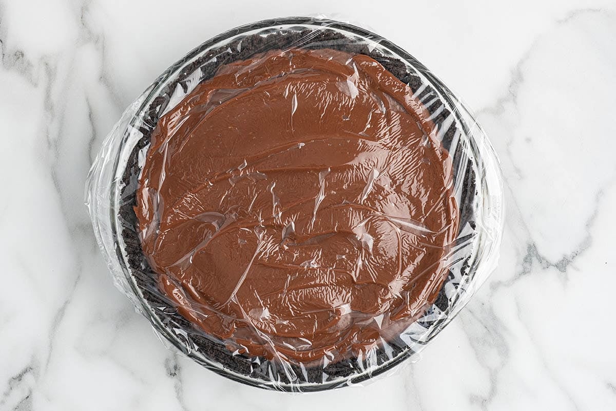 Chocolate layer set in the pie crust, covered with plastic wrap for chilling.