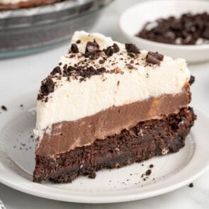 Slice of layered mud pie with Oreo crust, chocolate custard, and whipped cream on a plate.