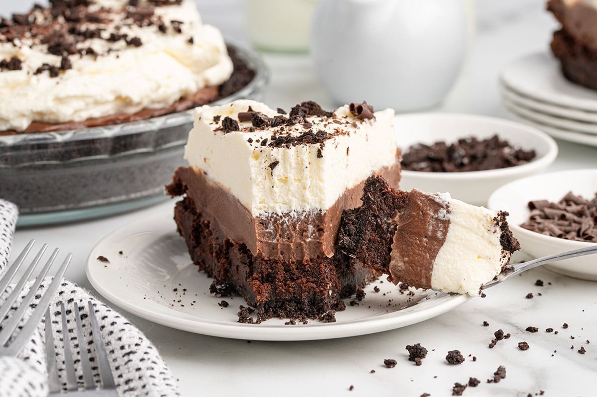 Slice of mud pie with a forkful lifted, showing the layered chocolate and whipped cream.
