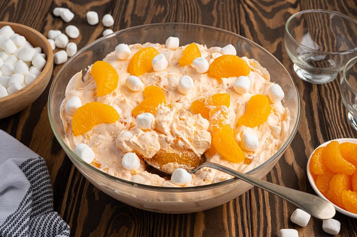 Creamy orange creamsicle salad topped with mandarin oranges and mini marshmallows in a large glass serving bowl.