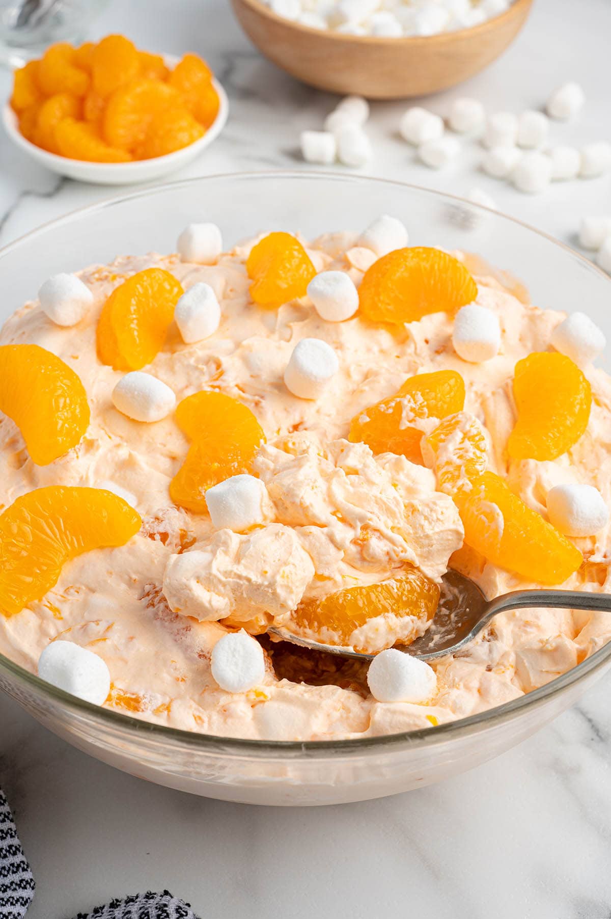 Creamy orange creamsicle salad topped with mandarin oranges and mini marshmallows, with a spoon scooping out a serving.