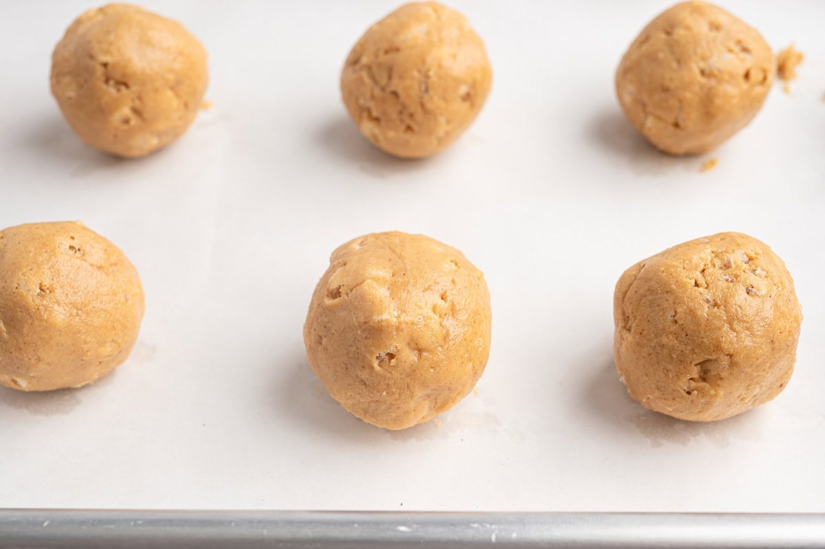 Rolled peanut butter Rice Krispie balls on a parchment-lined baking sheet before dipping.