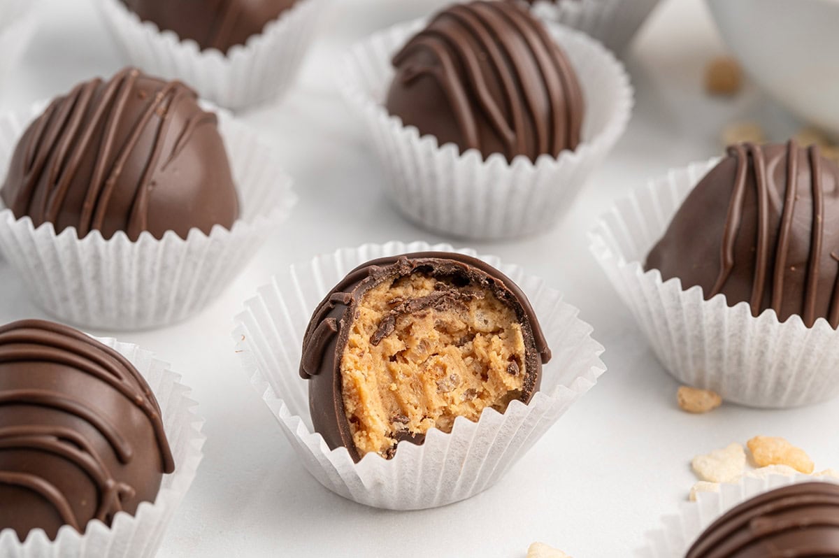 Chocolate peanut butter Rice Krispie balls in mini paper liners, one bitten open.