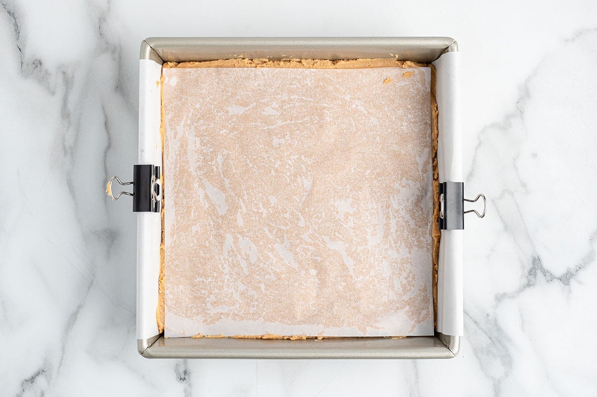Peanut butter fudge pressed into a parchment lined baking pan.