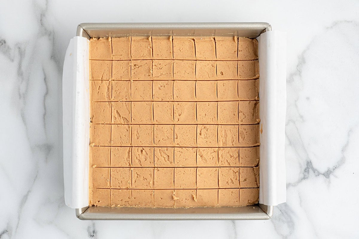 Scored peanut butter fudge in a parchment lined baking pan.