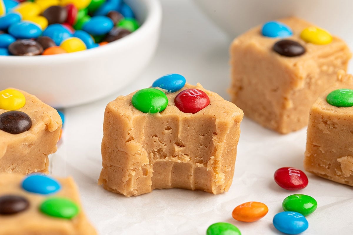 Peanut butter fudge square with a bite taken out, topped with colorful M&M's candies.