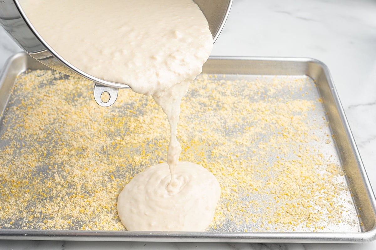 Pizza dough being poured onto a cornmeal dusted sheet pan.