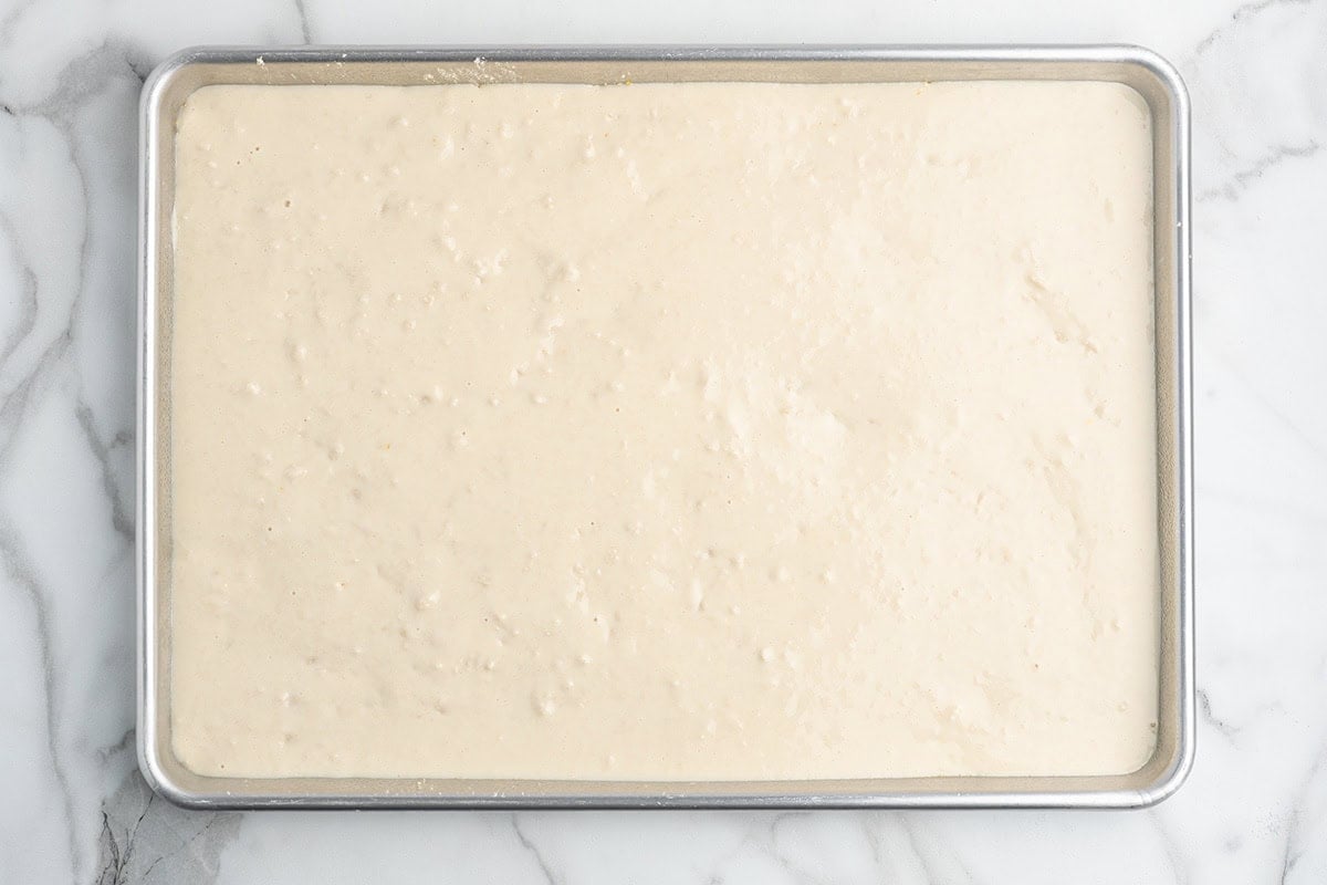 Pizza dough spread evenly in a sheet pan before baking.
