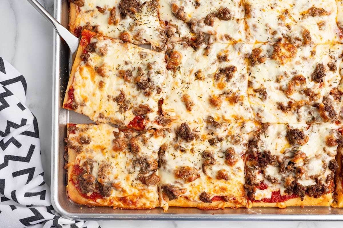 School pizza squares topped with melted cheese and sausage on a sheet pan.