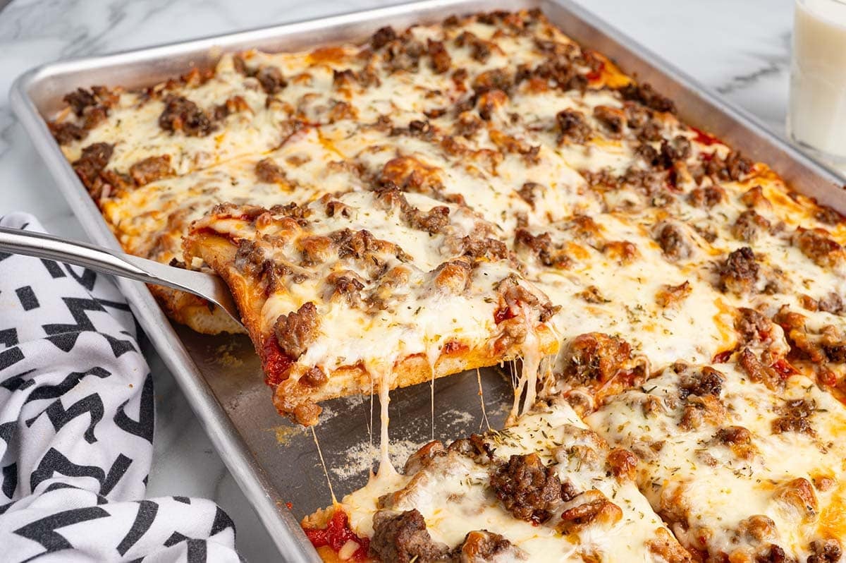 Sheet pan school pizza with a cheesy slice being served.
