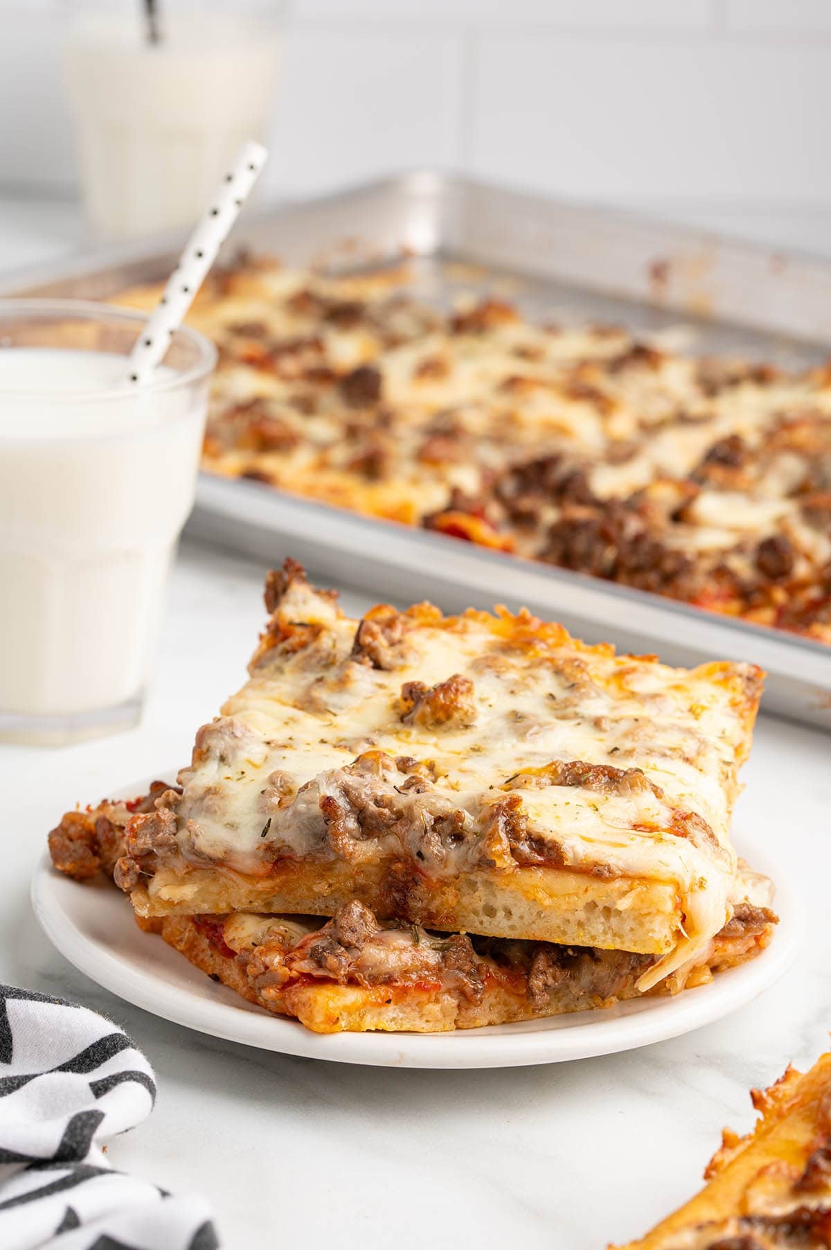 School pizza slices stacked on a plate with glasses of milk.