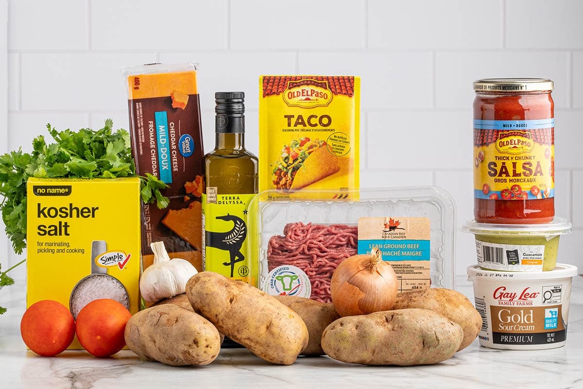 Taco Potato ingredients laid out including russet potatoes, ground beef, taco seasoning, salsa, sour cream, guacamole, cheddar cheese, tomatoes, onion, garlic, and cilantro.