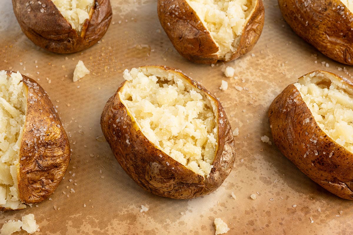 Freshly baked russet potatoes split open showing fluffy interiors on a parchment-lined baking sheet.
