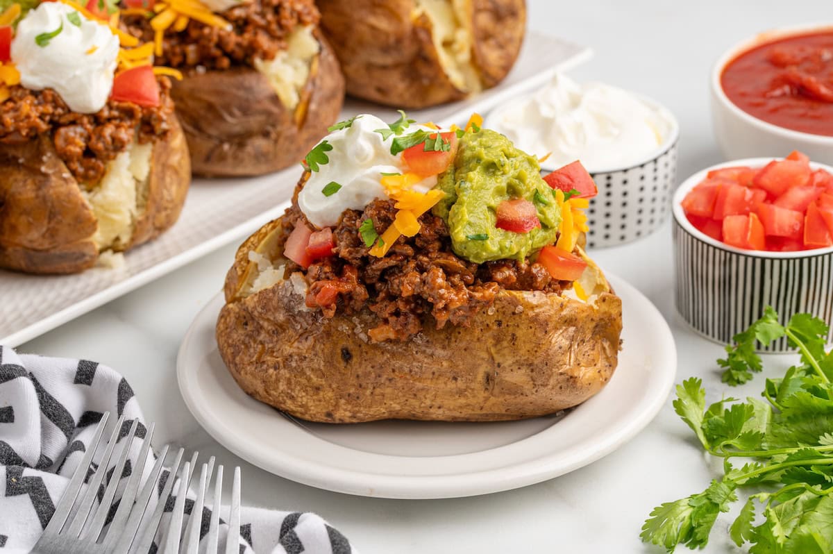A Taco Potato baked potato topped with seasoned ground beef, guacamole, sour cream, shredded cheddar, diced tomatoes, and cilantro.
