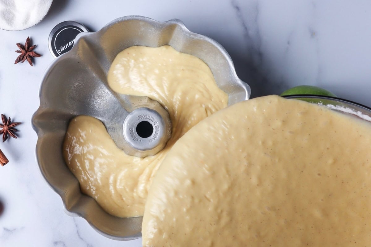 Cake batter being poured into a Bundt pan, with star anise and cinnamon sticks nearby.