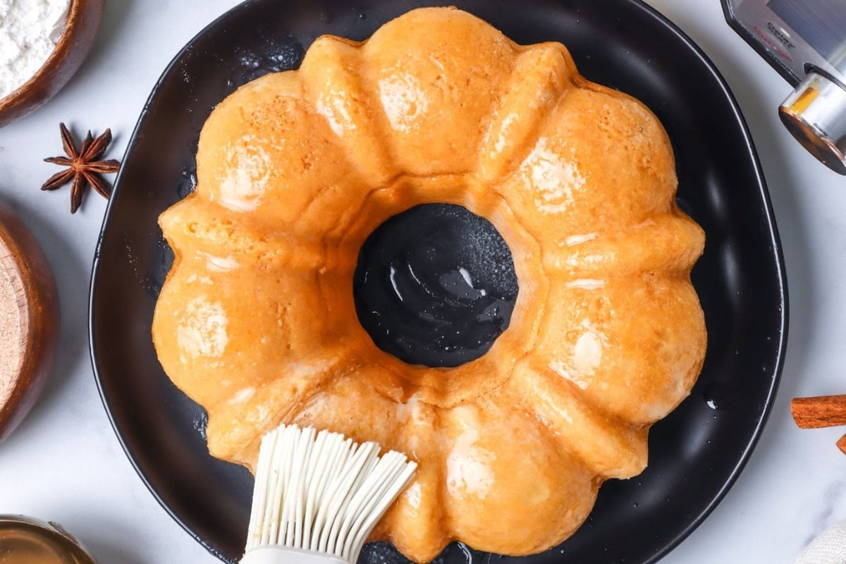 Butter being brushed onto a Bundt cake on a black plate, viewed from above.