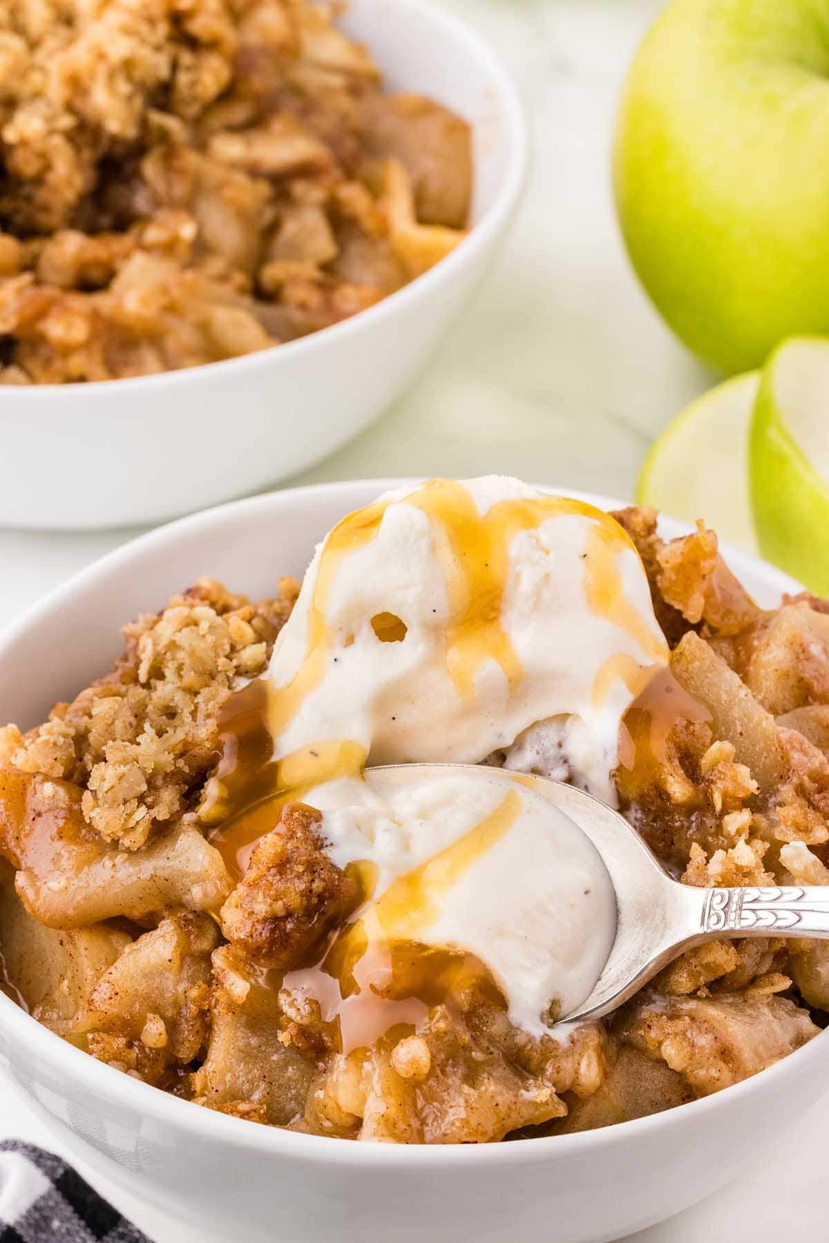Spoonful of apple crisp with ice cream and caramel lifted from a bowl.
