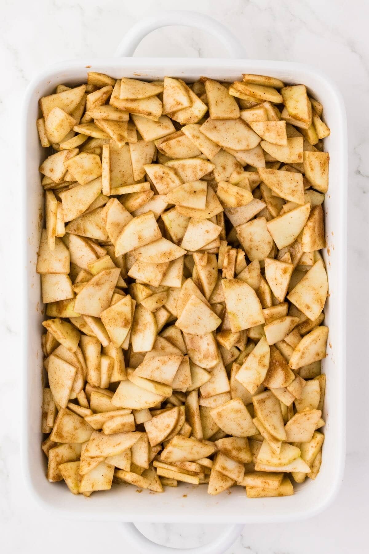 Cinnamon spiced apple slices in a white baking dish before adding the crumble topping.