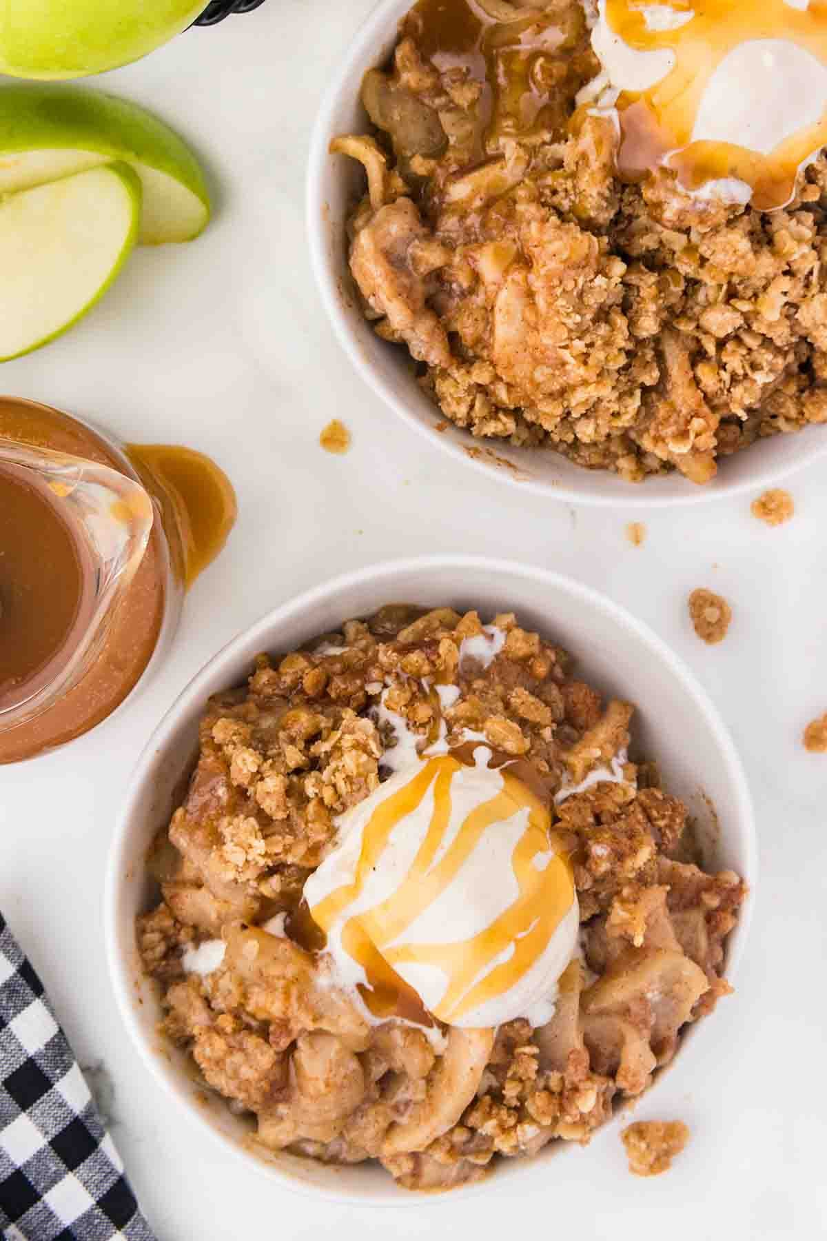 Overhead view of two bowls of apple crisp topped with ice cream and caramel drizzle.
