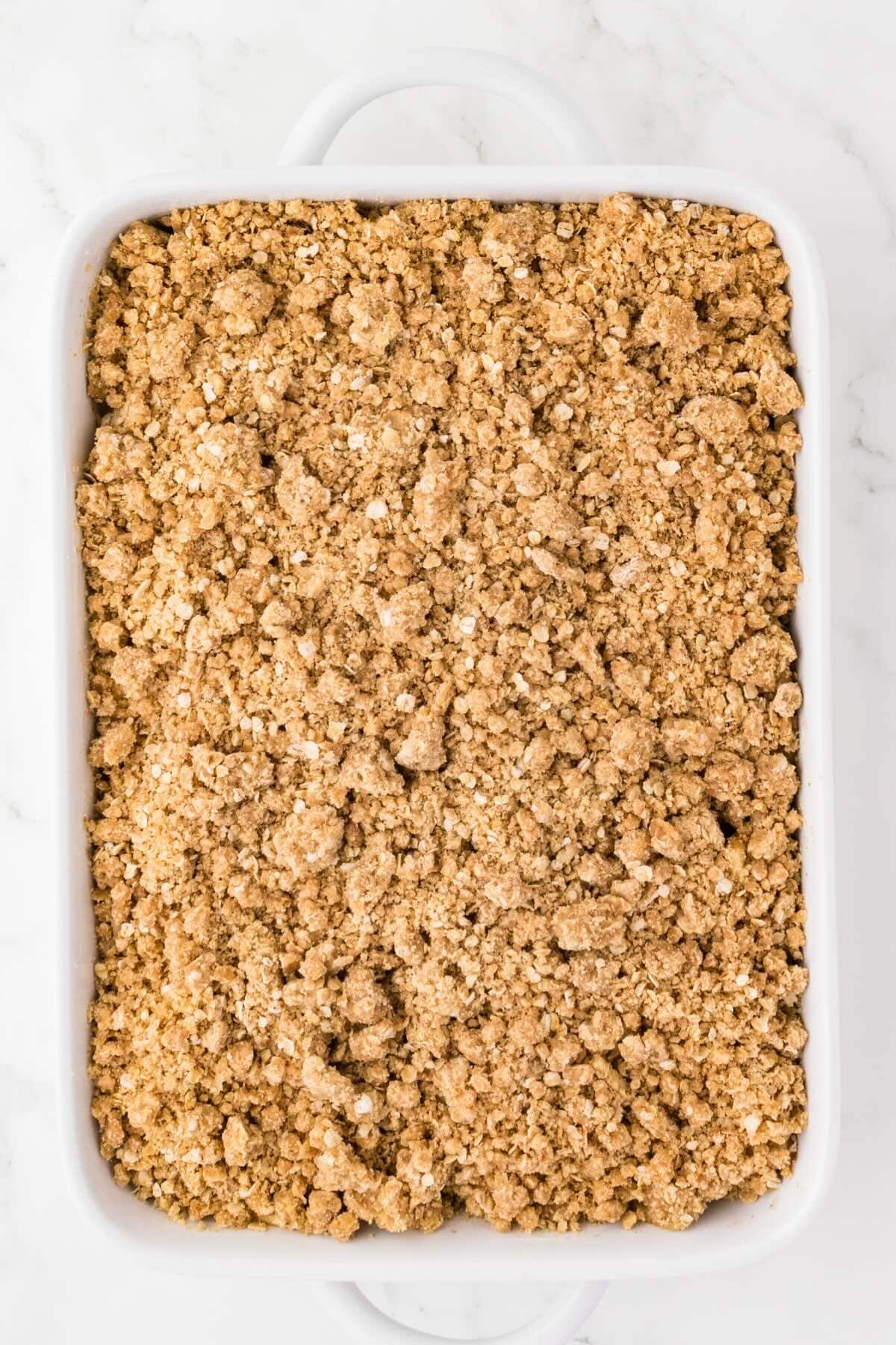 Oat crumble topping spread over apples in a baking dish before baking.