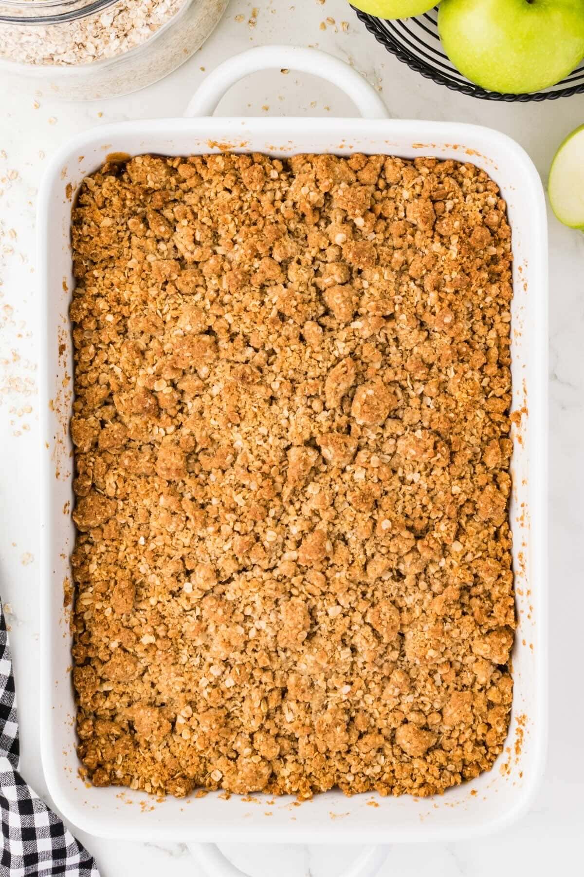 Baked apple crisp with golden oat crumble topping in a white baking dish.
