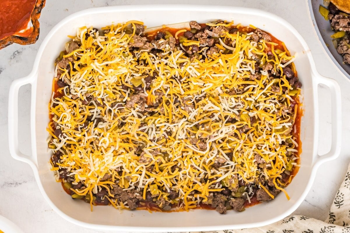 Beef enchilada casserole layered with beef filling and shredded cheese.