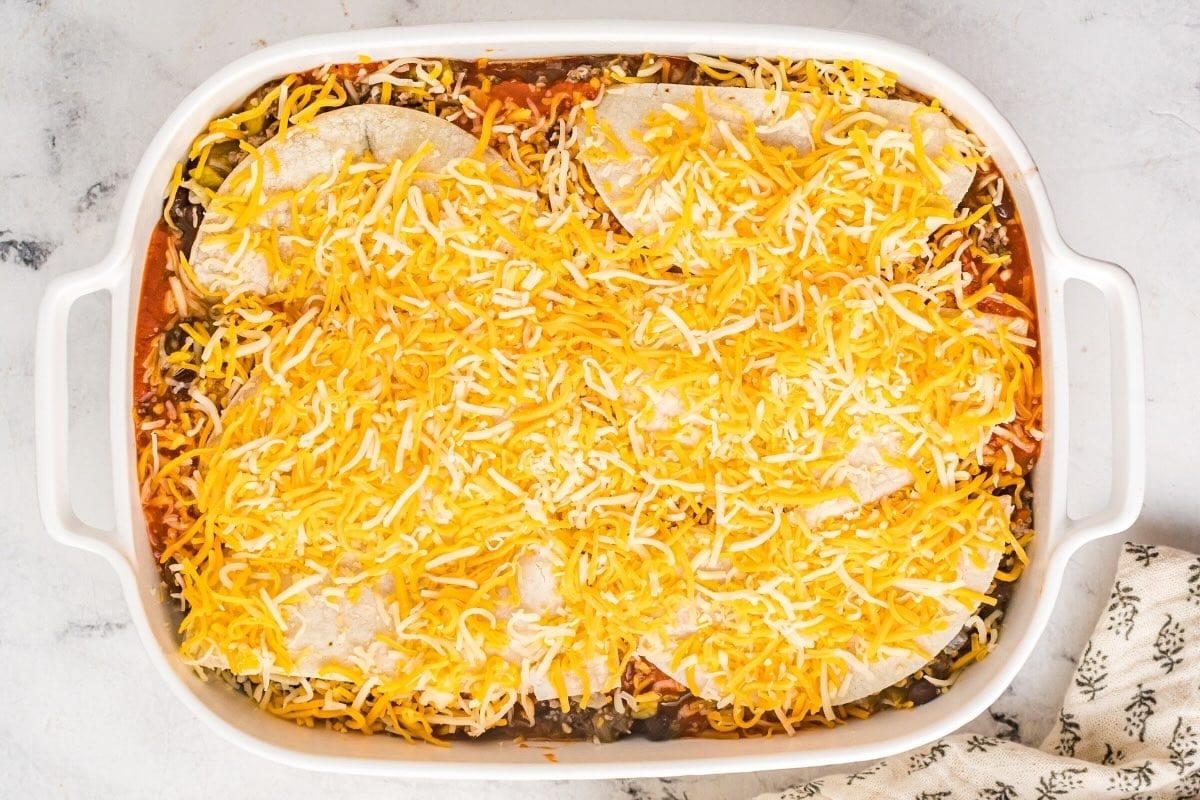 Beef enchilada casserole topped with tortillas and shredded cheese before baking.