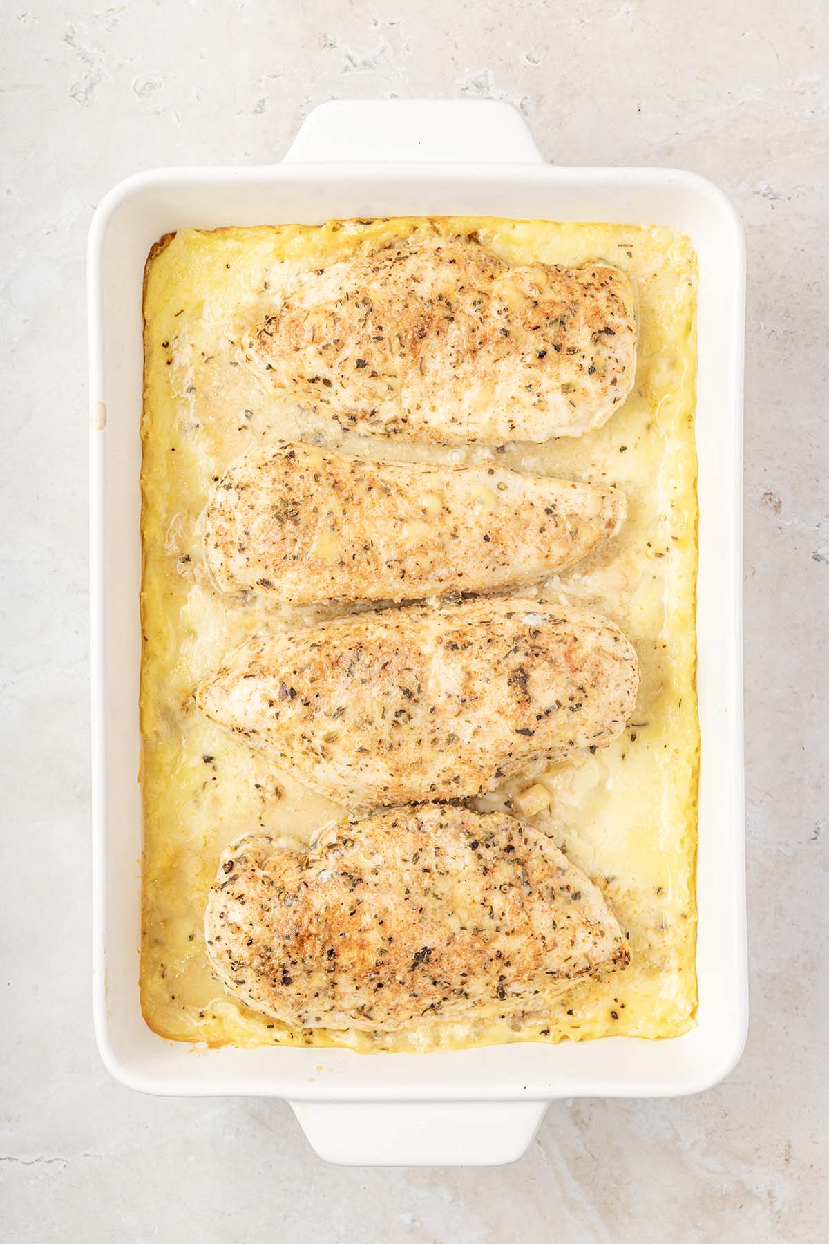Overhead view of freshly baked seasoned chicken breasts on top of creamy rice casserole in a white dish.