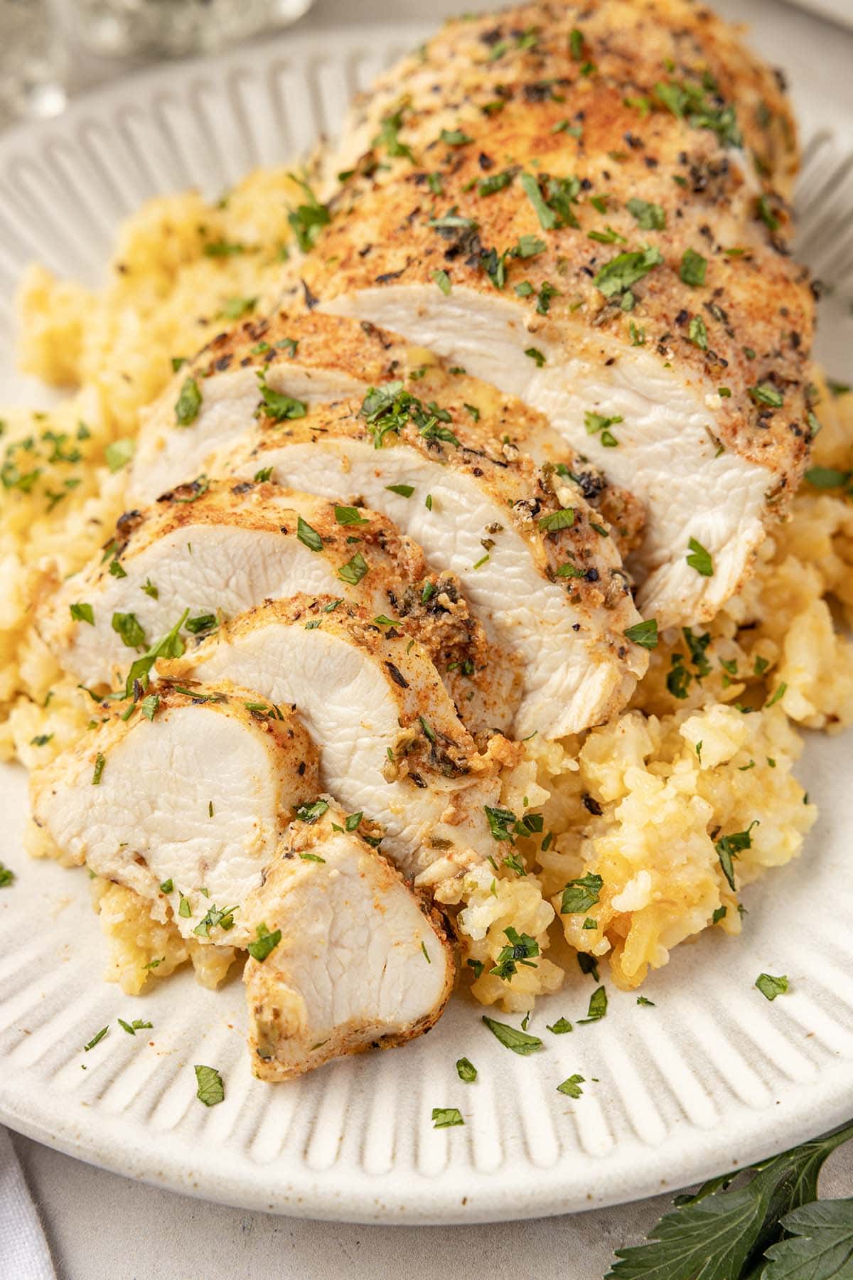 Sliced seasoned chicken breast plated over cheesy yellow rice, garnished with fresh parsley.