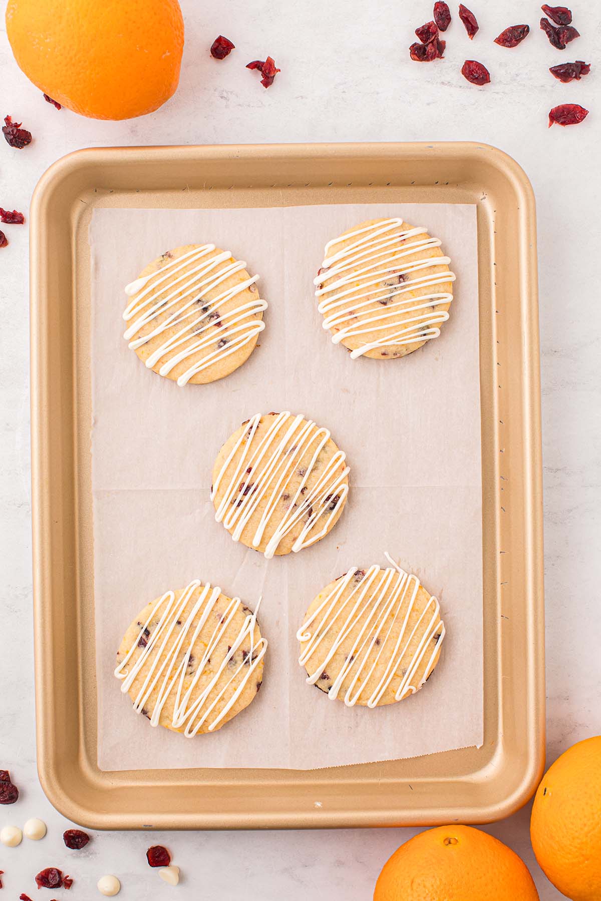 White chocolate-drizzled cranberry orange shortbread cookies on a parchment-lined baking sheet.