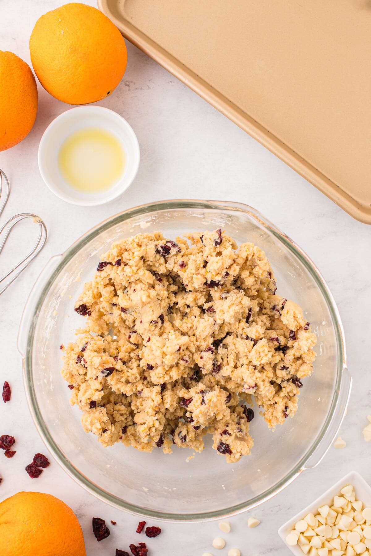 Cranberry orange shortbread cookie dough mixed in a glass bowl with oranges nearby.