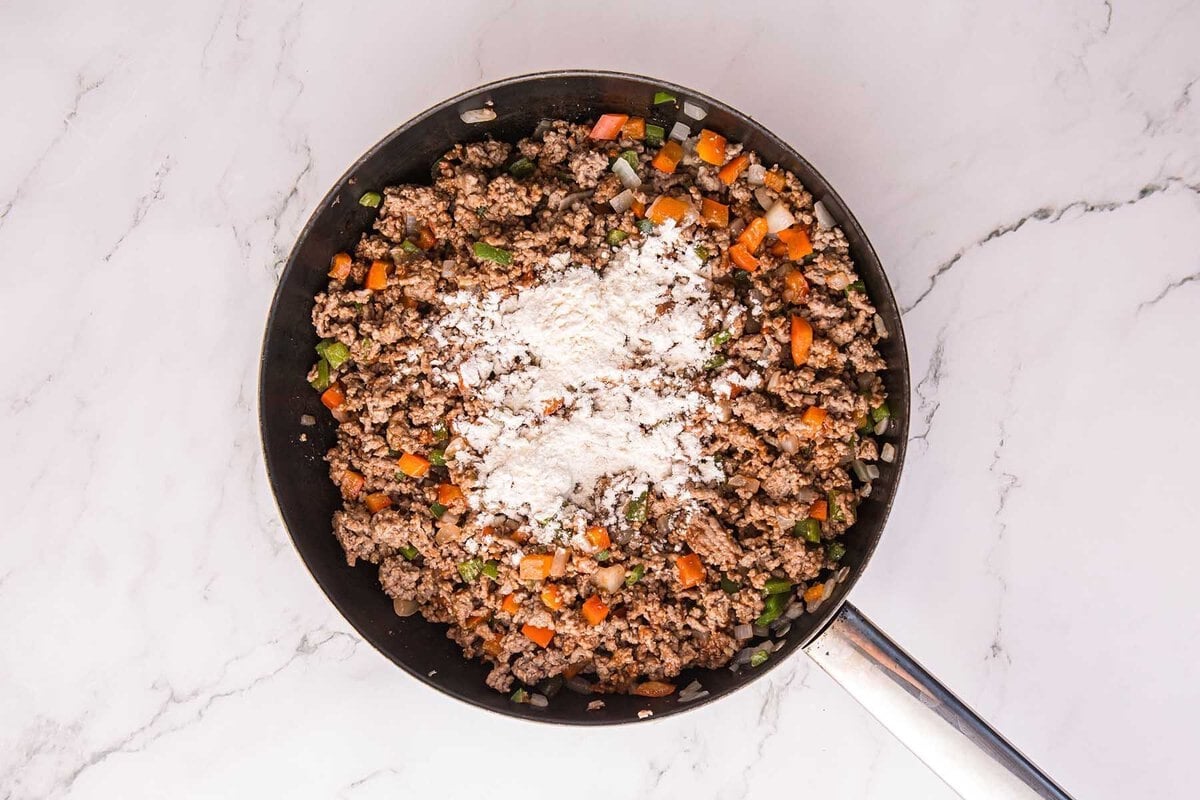 Dirty Spaghetti ground beef and diced vegetables topped with flour in a skillet.