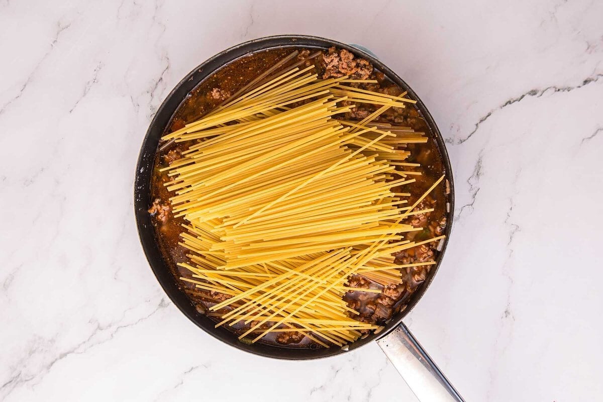 Dirty Spaghetti with uncooked spaghetti added to the ground beef mixture in a skillet.