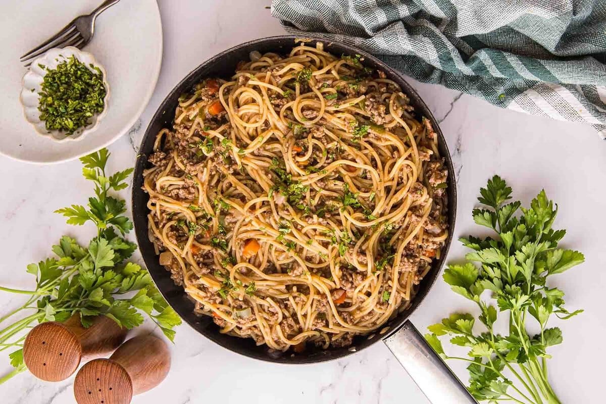 Dirty Spaghetti with ground beef and vegetables in a skillet, topped with chopped parsley.