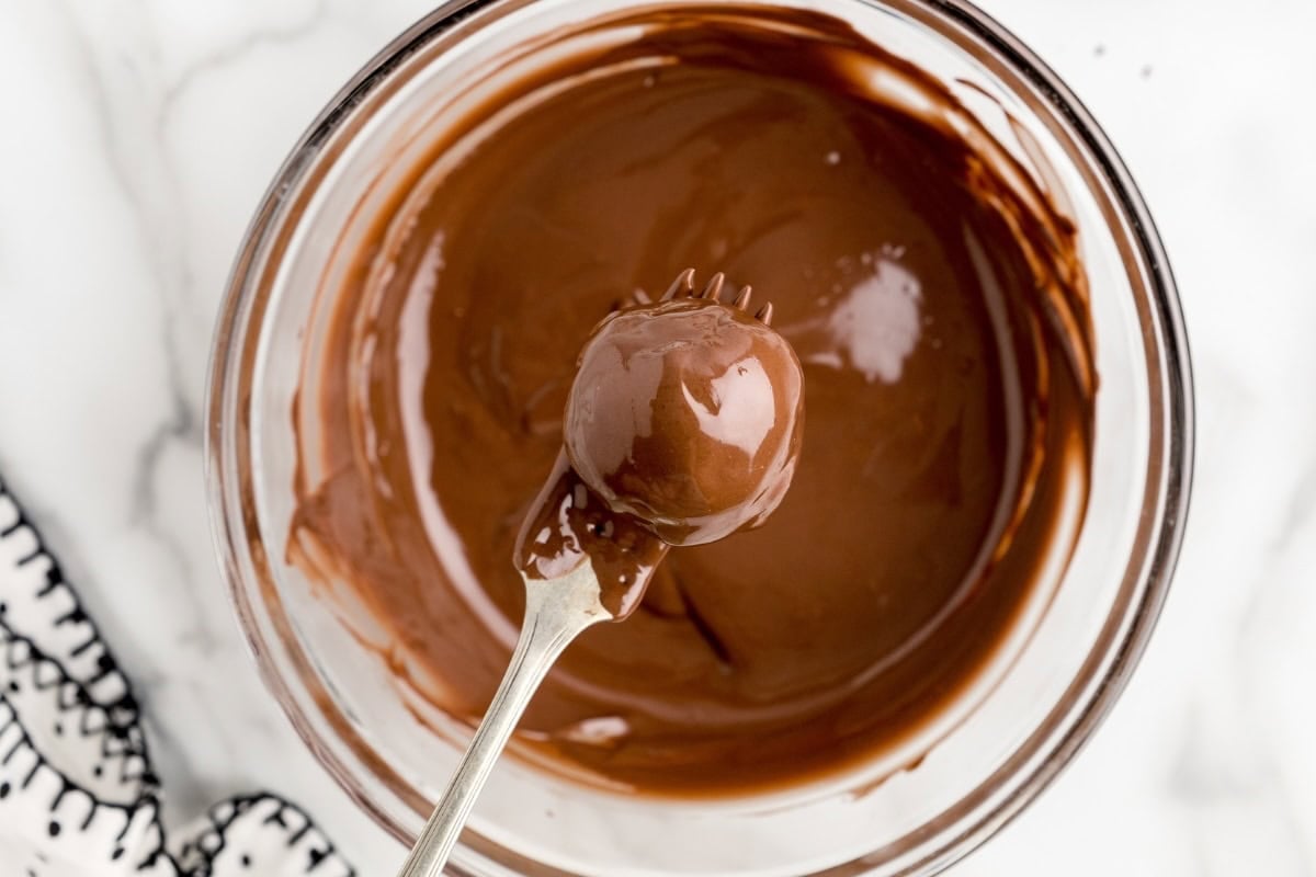 Pecan Pie Ball being dipped in melted chocolate with a fork.