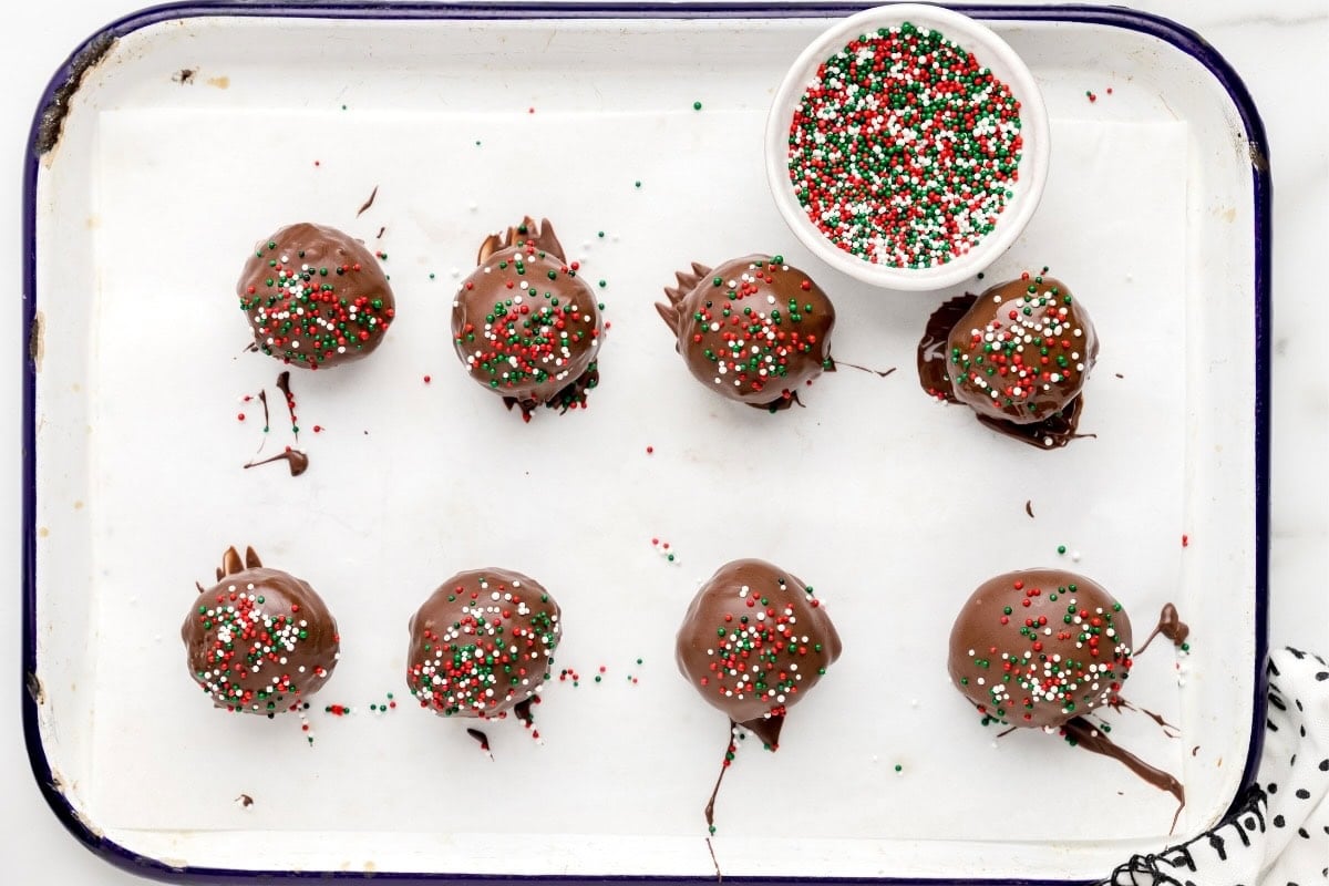 Pecan Pie Balls coated in chocolate with Christmas sprinkles on a baking tray.