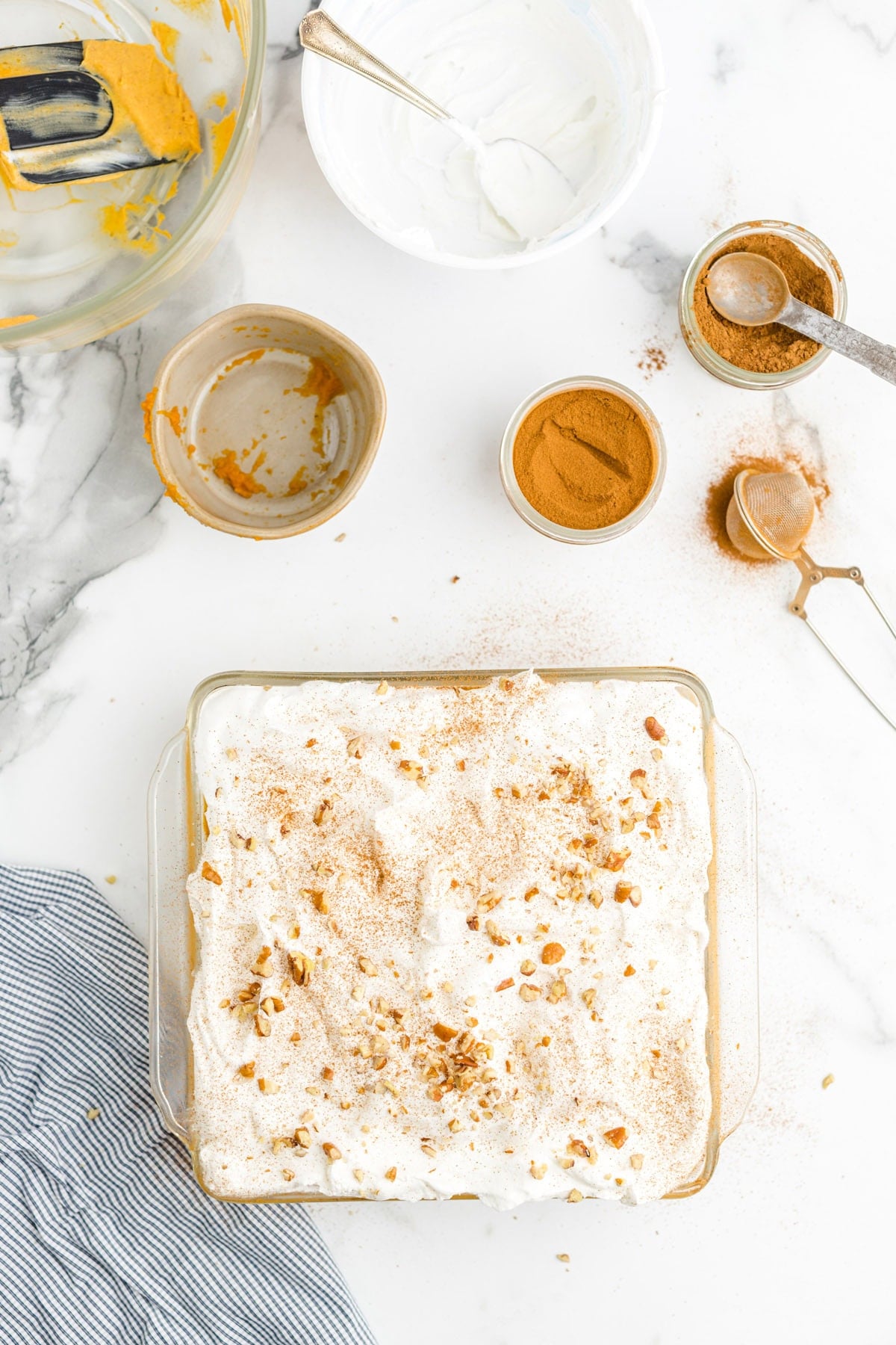 Assembled pumpkin delight dessert topped with whipped cream, chopped nuts, and a cinnamon dusting in a baking dish.