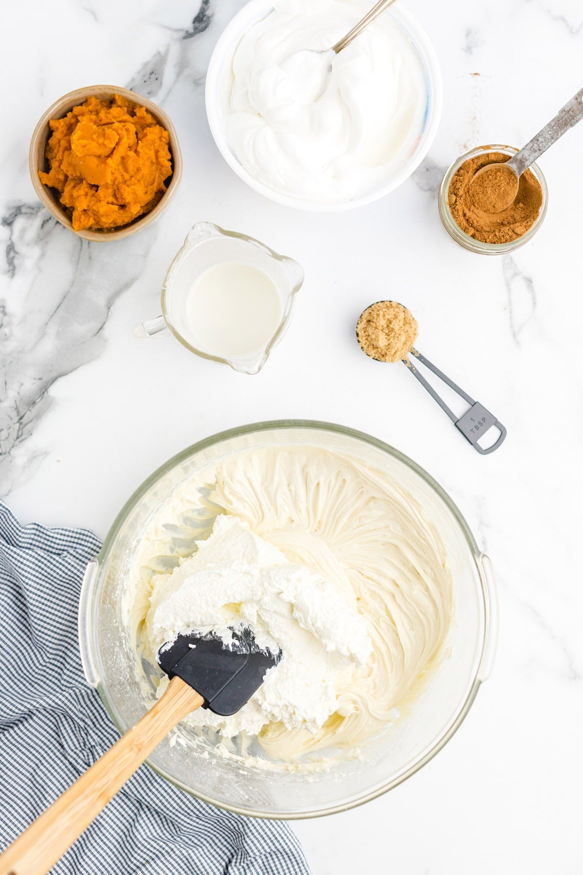 Whipped cream cheese mixture in a glass bowl, surrounded by pumpkin puree, whipped topping, milk, cinnamon, and brown sugar.