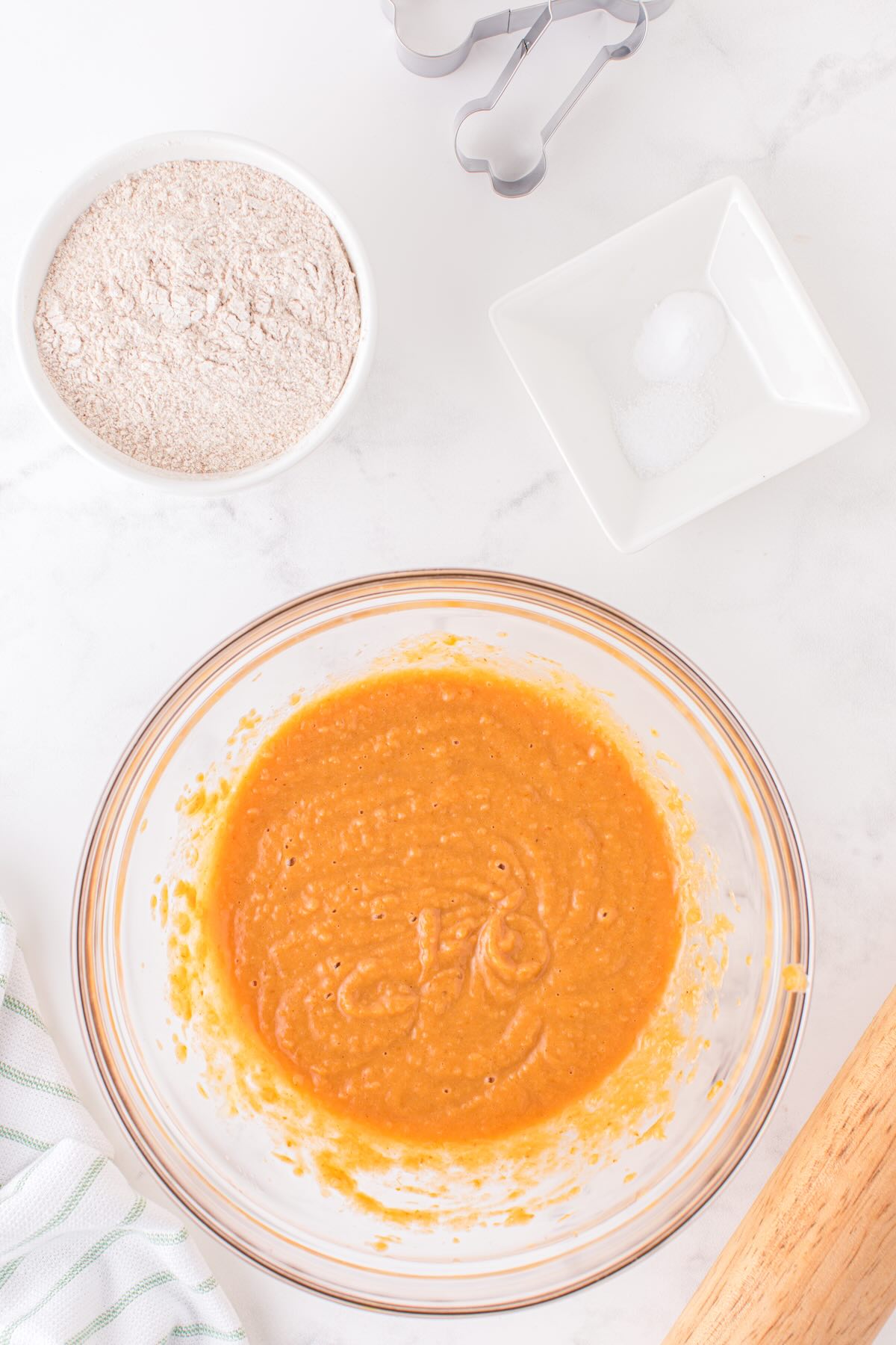 Pumpkin dog treat batter in a glass bowl with flour and salt nearby.