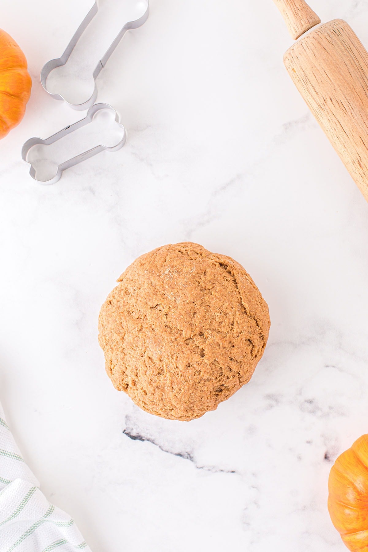 Ball of pumpkin dog treat dough on a marble surface with bone-shaped cutters.